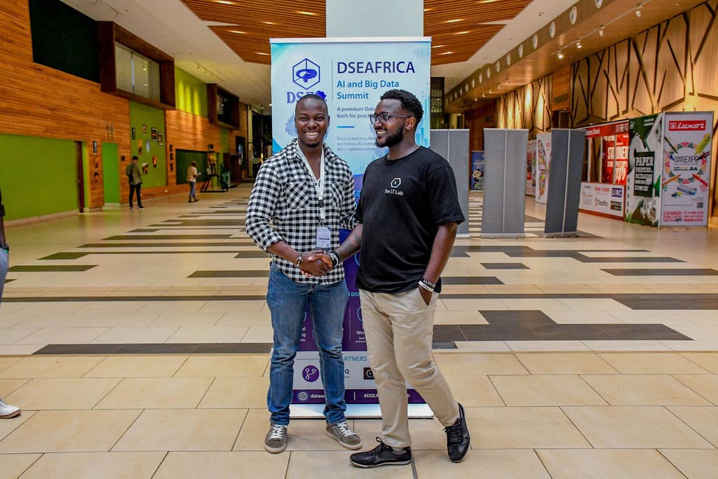 Two attendees shaking hands beside the summit banner